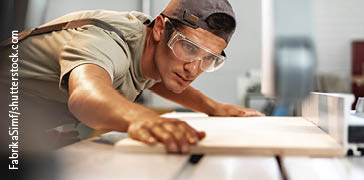 Ein Mann bearbeitet ein Stueck Holz praezise und genau mit fachkundigem Blick
