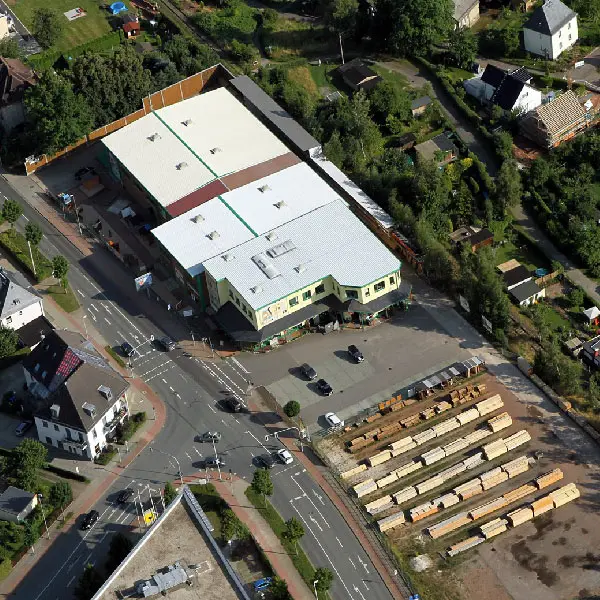 Ansicht aus der Vogelperspektive auf ein zweigeschossiges Verkaufsgebäude mit Lagerhalle und Parkplatz.