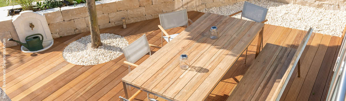 Moderne Kombination aus Gartenstühlen und Tisch mit Holzarmlehnen und Holztischplatte stehen auf einer geriffelten Holzterrasse bei sonnigem Wetter