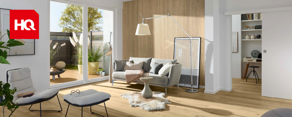 Modern eingerichteter Raum mit weissen Akzenten, Holzboden, Akustikpaneelen an der Wand und grosser Terrassentür mit Blick auf die Terrasse.