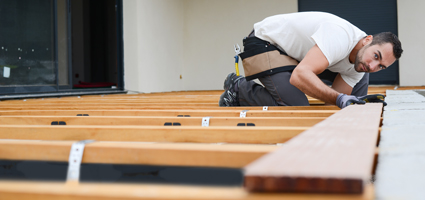 Handwerker platziert eine Terrassendiele auf einer hölzernen Unterkonstruktion.