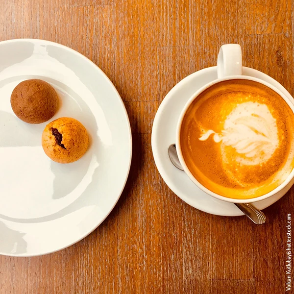 Hölzerne Tischplatte mit Kaffeetasse und Teller mit Süßigkeiten.