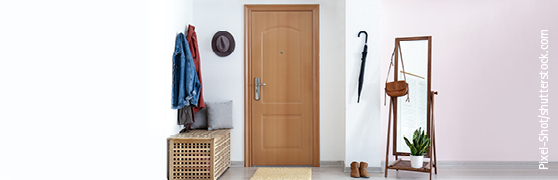 Hölzerne Wohnungseingangstür in weißem Raum mit Garderobe, Spiegel und Schirm.