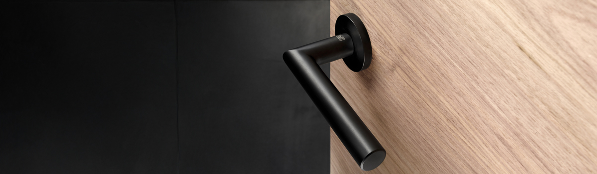 schwarzer Tuergriff in geradliniger Form an einer quergemaserten Holztuer